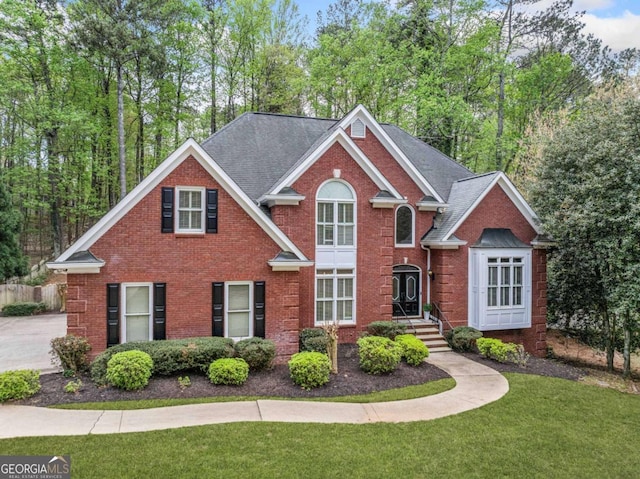 traditional-style home featuring brick siding, a front yard, and roof with shingles
