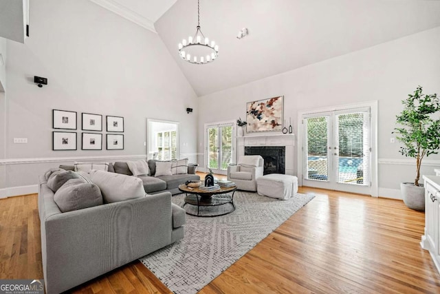 living area with high vaulted ceiling, a chandelier, light wood-style floors, a high end fireplace, and baseboards