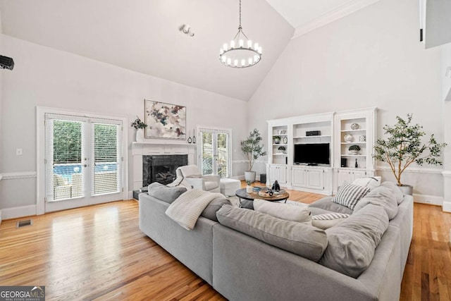 living area featuring high vaulted ceiling, a fireplace, a chandelier, light wood-type flooring, and baseboards