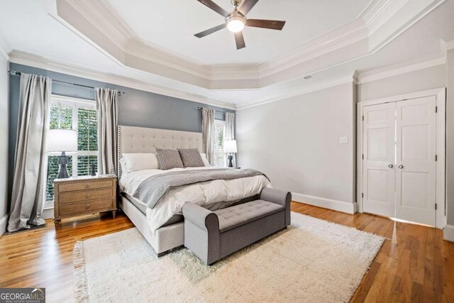 bedroom featuring a raised ceiling, ornamental molding, wood finished floors, and ceiling fan