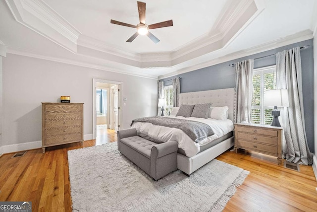 bedroom with a tray ceiling, multiple windows, crown molding, light wood-type flooring, and baseboards