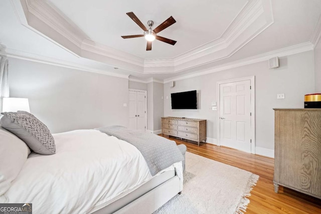 bedroom featuring a raised ceiling, light wood finished floors, ornamental molding, baseboards, and ceiling fan