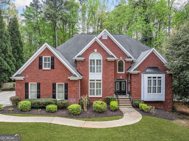 traditional home with brick siding, a front yard, and roof with shingles