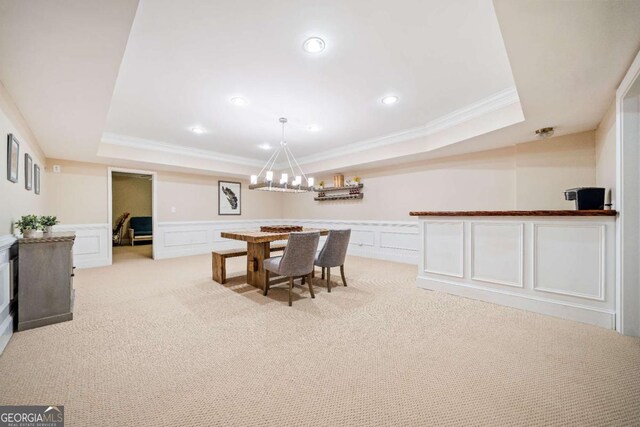 dining space featuring crown molding, a decorative wall, a raised ceiling, light colored carpet, and a chandelier