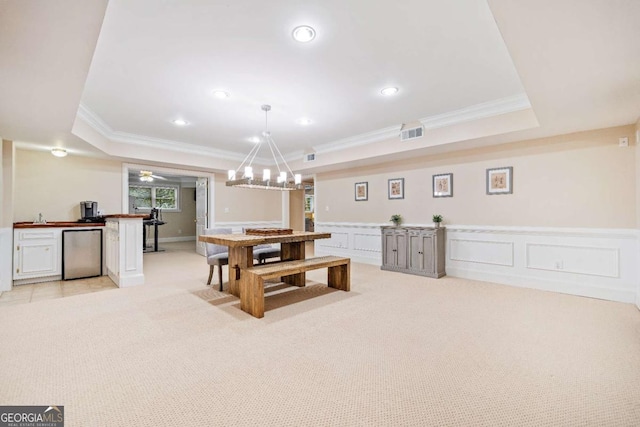 recreation room featuring crown molding, a tray ceiling, light carpet, wainscoting, and a decorative wall