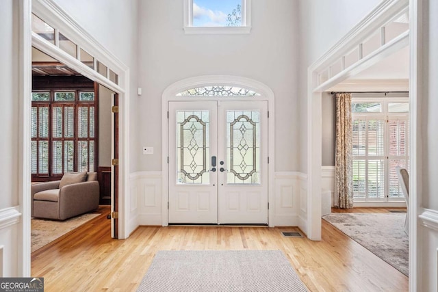 foyer featuring wood finished floors, plenty of natural light, a wainscoted wall, french doors, and a high ceiling