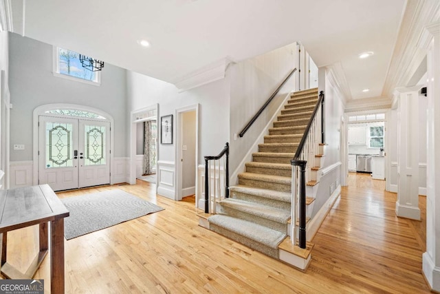 entrance foyer with stairway, healthy amount of natural light, wood finished floors, crown molding, and wainscoting
