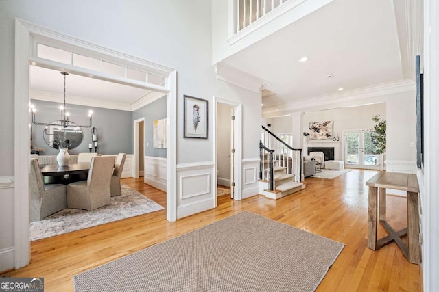 entrance foyer featuring stairway, ornamental molding, wood finished floors, a chandelier, and wainscoting