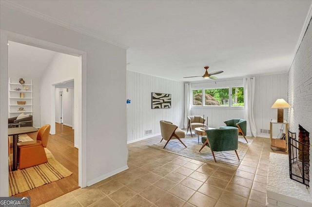 living room featuring ornamental molding, a ceiling fan, baseboards, and a brick fireplace