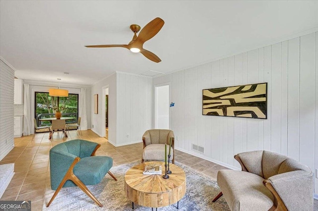 living area featuring light tile patterned floors, crown molding, a ceiling fan, and baseboards