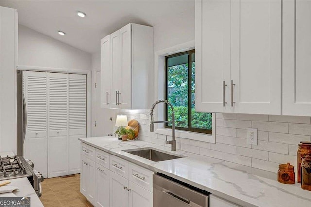 kitchen featuring appliances with stainless steel finishes, a sink, white cabinets, light stone counters, and tasteful backsplash