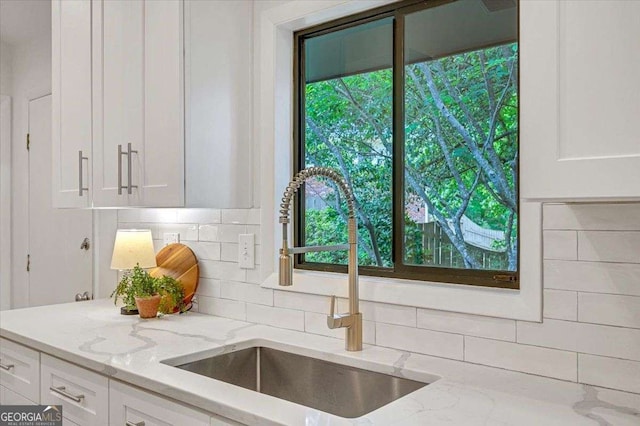 kitchen view of a sink, white cabinets, decorative backsplash, and light stone counters