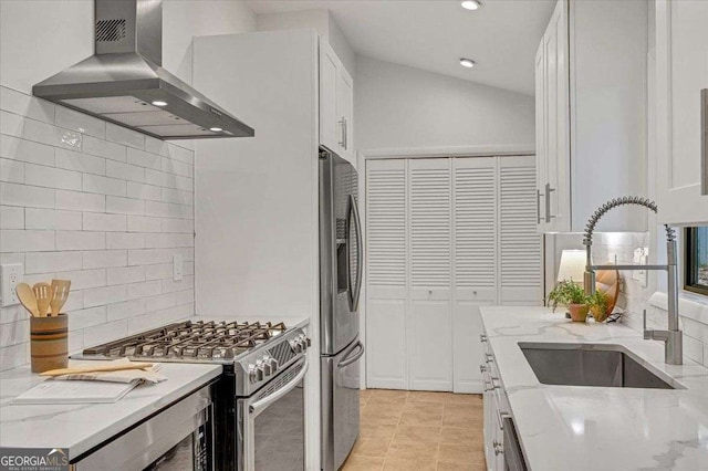 kitchen featuring wall chimney exhaust hood, appliances with stainless steel finishes, a sink, tasteful backsplash, and white cabinets