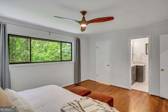 bedroom featuring light wood-style flooring, crown molding, baseboards, a sink, and ensuite bathroom