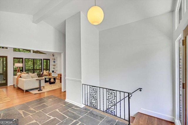 hall featuring high vaulted ceiling, an upstairs landing, beamed ceiling, wood finished floors, and baseboards