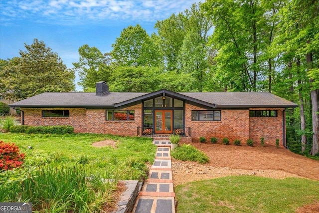view of front of property with french doors, a chimney, brick siding, and a front yard