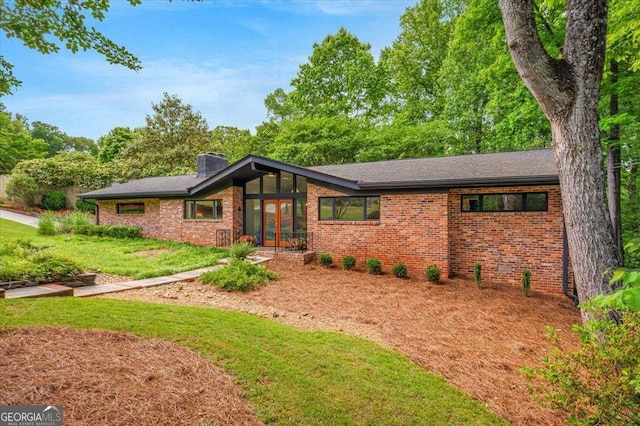 view of front of house featuring brick siding, a chimney, french doors, and a front yard