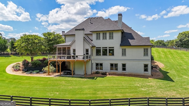 rear view of house with a chimney, a sunroom, a patio area, a wooden deck, and roof with shingles
