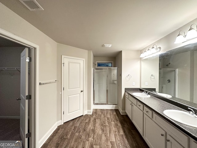 full bath featuring a sink, double vanity, a shower stall, and wood finished floors