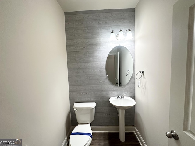 bathroom with toilet, wood finished floors, baseboards, and wood walls
