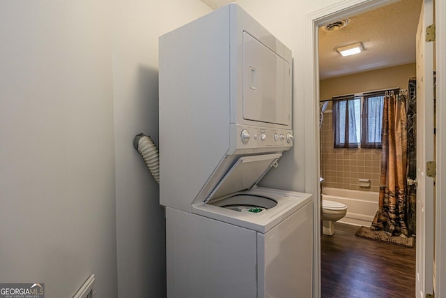 clothes washing area featuring a textured ceiling, visible vents, stacked washing maching and dryer, dark wood-type flooring, and laundry area