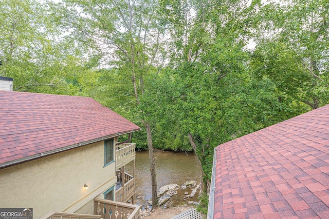 details featuring roof with shingles, a water view, and stucco siding