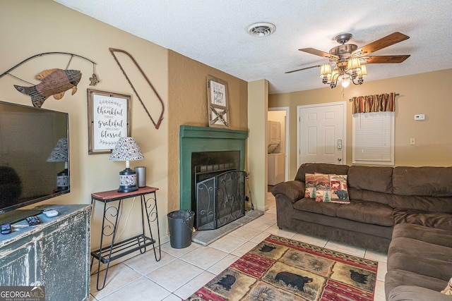 living area featuring light tile patterned floors, a fireplace with raised hearth, ceiling fan, and a textured ceiling