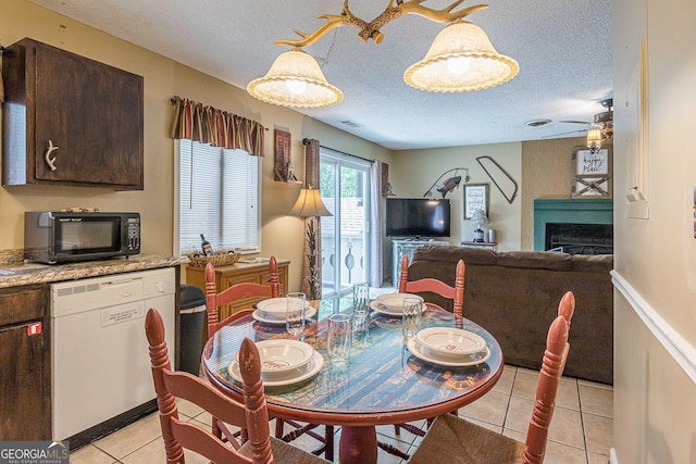 dining space with a ceiling fan, a fireplace, a textured ceiling, visible vents, and light tile patterned flooring