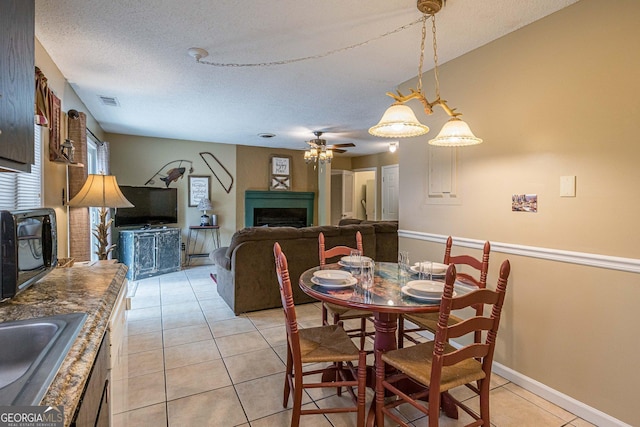 dining room featuring a ceiling fan, a textured ceiling, visible vents, light tile patterned flooring, and a fireplace