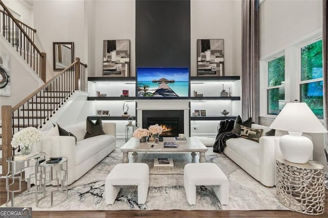 living area featuring stairs, a towering ceiling, a warm lit fireplace, and wood finished floors