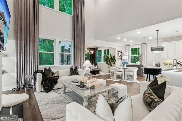 living area with light wood finished floors, recessed lighting, a towering ceiling, a chandelier, and crown molding