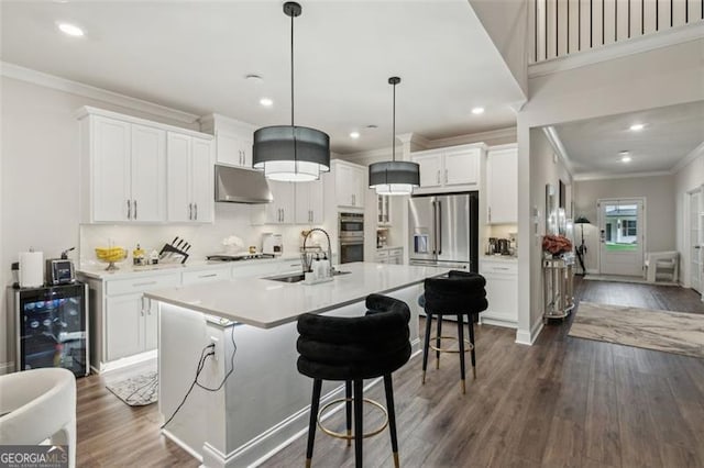 kitchen with stainless steel appliances, a sink, wine cooler, crown molding, and under cabinet range hood