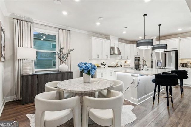 kitchen featuring stainless steel appliances, a center island with sink, wood finished floors, a sink, and crown molding