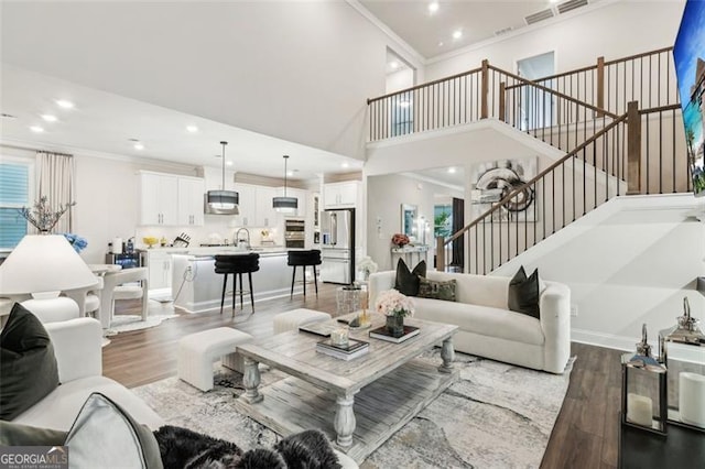 living room with wood finished floors, stairway, ornamental molding, recessed lighting, and a towering ceiling