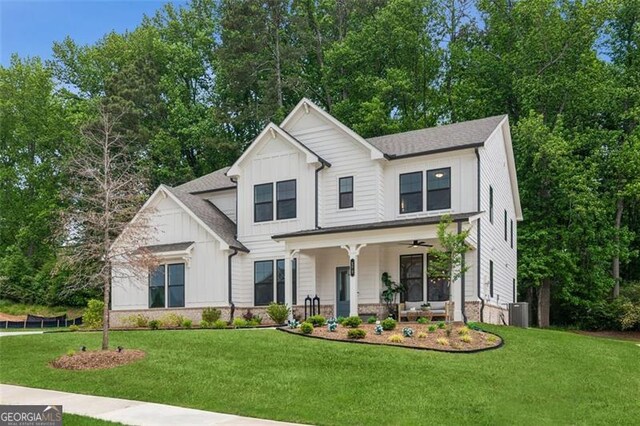 modern inspired farmhouse with board and batten siding, covered porch, a front yard, and central air condition unit