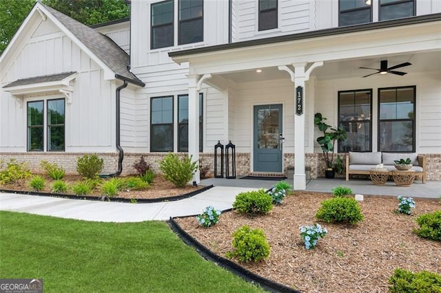 doorway to property featuring board and batten siding, brick siding, a ceiling fan, and covered porch