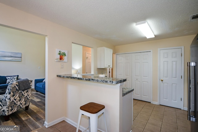 kitchen with white cabinetry, a breakfast bar area, light tile patterned flooring, a peninsula, and a textured ceiling