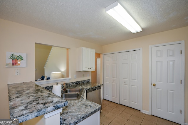 kitchen featuring stainless steel dishwasher, white cabinets, light tile patterned floors, a sink, and a textured ceiling