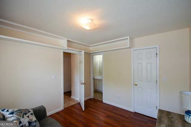 unfurnished bedroom featuring wood finished floors, connected bathroom, baseboards, and a textured ceiling