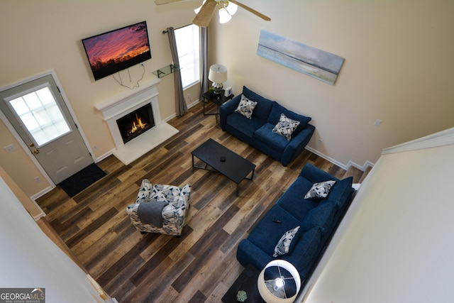 living area featuring a warm lit fireplace, baseboards, wood finished floors, and a ceiling fan