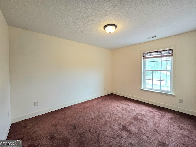 empty room with dark colored carpet, a textured ceiling, baseboards, and visible vents