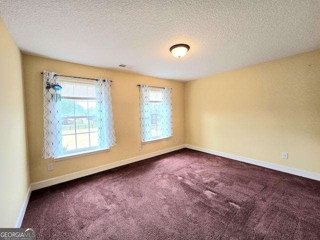 spare room featuring a textured ceiling, visible vents, baseboards, and dark carpet
