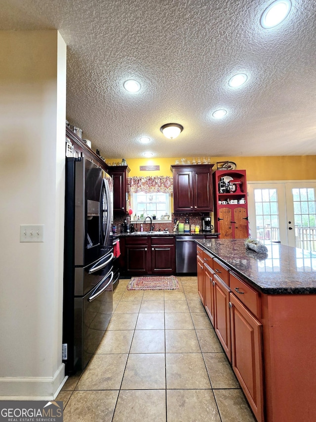 kitchen featuring stainless steel dishwasher, a wealth of natural light, a textured ceiling, and black fridge