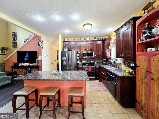 kitchen with a breakfast bar area, a center island, a sink, a textured ceiling, and appliances with stainless steel finishes