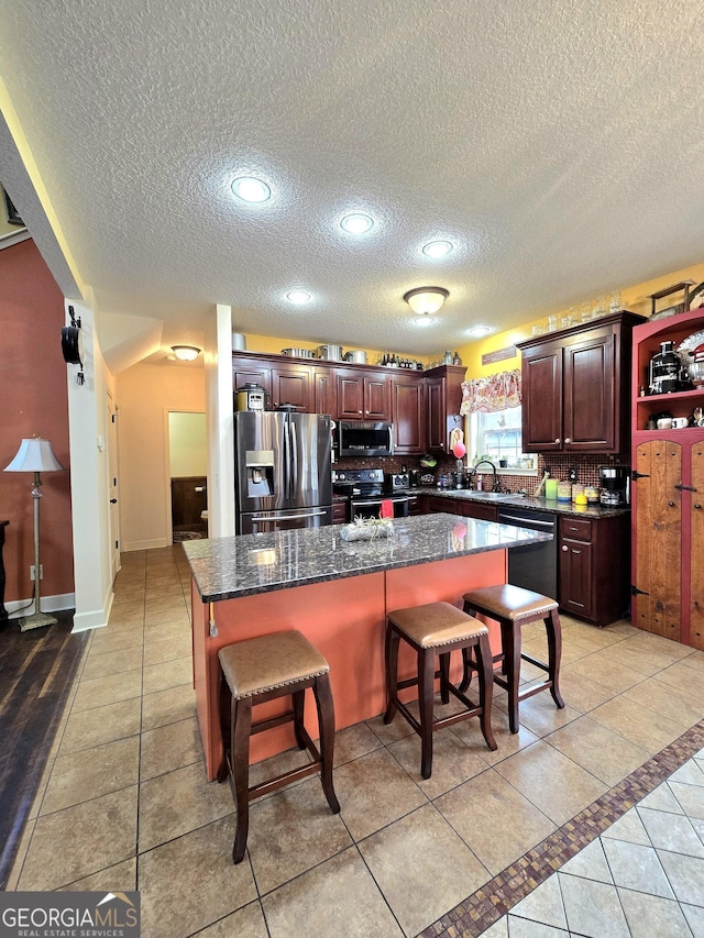 kitchen featuring light tile patterned floors, stainless steel appliances, a textured ceiling, and a kitchen island