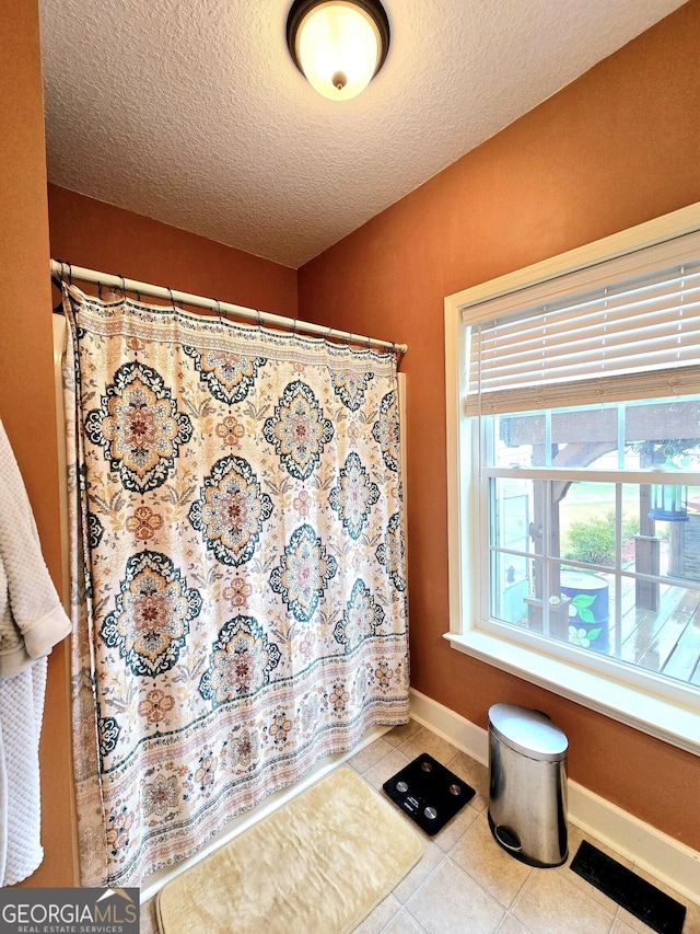 interior space featuring baseboards, tile patterned flooring, a textured ceiling, and curtained shower