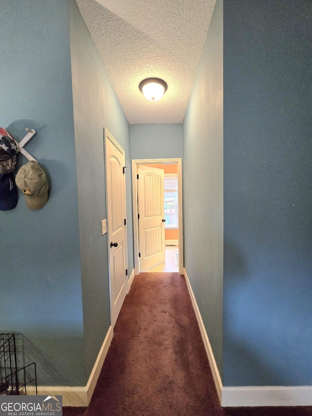 hallway featuring a textured ceiling, baseboards, and carpet floors