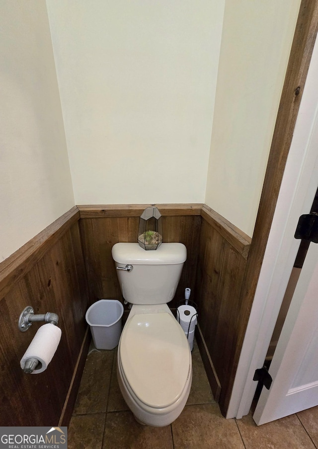 bathroom with toilet, tile patterned flooring, wood walls, and a wainscoted wall