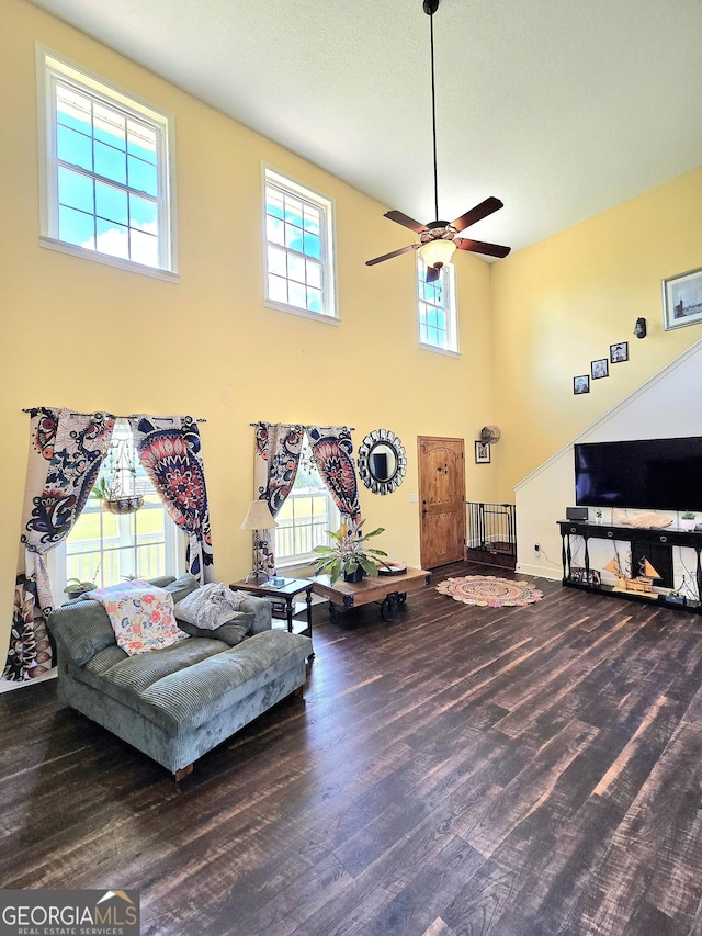 living room featuring a ceiling fan, baseboards, wood finished floors, and a towering ceiling