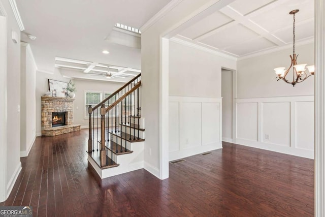 entrance foyer featuring coffered ceiling, a decorative wall, a stone fireplace, stairway, and ceiling fan